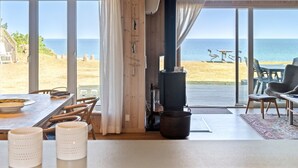Ein gemütliches Zimmer mit großem Fenster mit Blick auf einen Strand, einer Holzbalkendecke und einem rustikalen Ofen.