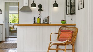 A kitchen with white paneling, a wooden counter, and a wicker chair with a colorful cushion. - "Gritt" - 800m from the sea by Interhome (Gilleleje)
