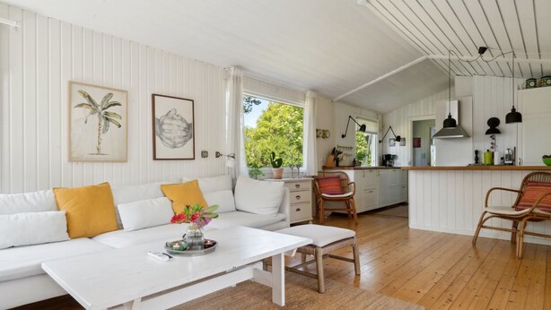 A spacious living area with a white sofa, a coffee table, and a kitchen area with wooden cabinets and a bar counter. - "Gritt" - 800m from the sea by Interhome (Gilleleje)