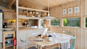 A wooden interior with a kitchen and dining area, including shelves, a table, chairs, and a hanging light fixture. - "Sjard" - 700m from the sea by Interhome (Gilleleje)