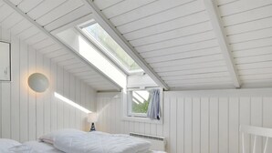 A bedroom with a sloped ceiling, a bed with white bedding, a chair, and a window with curtains.