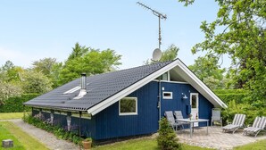 A small blue house with a sloped roof, a satellite dish, and a patio with two chairs and a table.