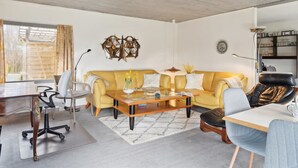 A modern living room with a yellow sofa, a wooden coffee table, and a desk with a chair.