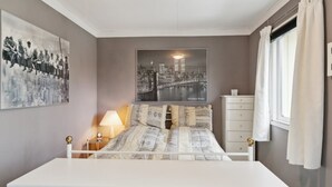 A bedroom with a bed, a nightstand, a lamp, a dresser, and a window with curtains.