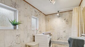 A bathroom with a marble wall, a washing machine, a bathtub, and a toilet.