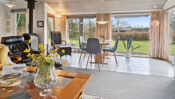 A modern living room with a fireplace, leather sofa, dining area, and large windows offering a view of the outdoors.
