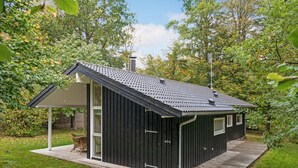 A small, dark-colored wooden building with a sloped roof, a covered porch, and a window.
