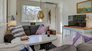A cozy living room with a round table, a sofa, a television, and a window with a view of trees.