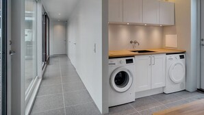 Ein moderner Waschraum mit integrierten Waschmaschinen und Trocknern, einer Holz Arbeitsplatte und weißen Schränken.