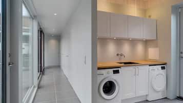 Une buanderie moderne dotée d’un lave-linge et d’un sèche-linge encastrés, d’un plan de travail en bois et de meubles blancs.