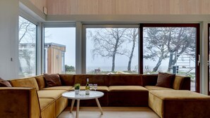 Ein modernes Wohnzimmer mit einem großen Ecksofa, einem runden Couchtisch und Meerblick durch große Fenster.