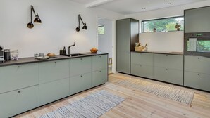 Ett modernt kök med en central köksö, två hänglampor och ett fönster med utsikt över grönområden.