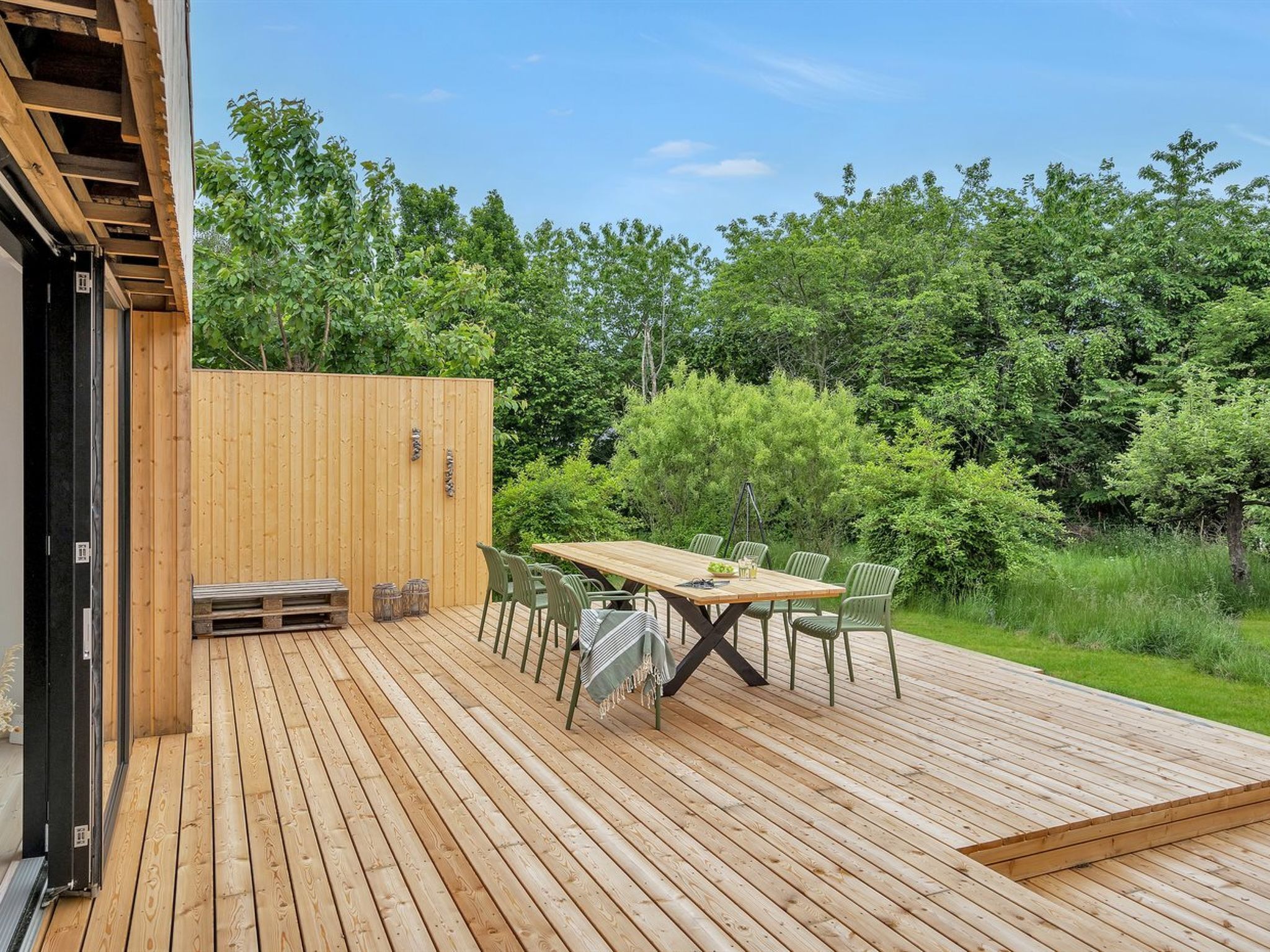 A wooden deck with a table and chairs, surrounded by greenery.