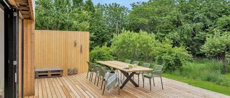 A wooden deck with a table and chairs, surrounded by greenery.