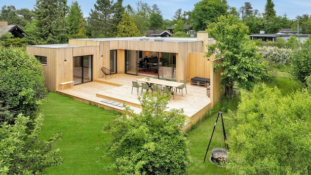 Ett modernt hus med en stor terrass, en matplats och ett kök som syns genom glasdörrar.
