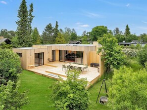 Una casa moderna con una amplia terraza, un comedor y una cocina visibles a través de puertas de vidrio.