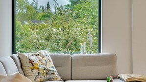 Ett modernt vardagsrum med en soffa, ett soffbord och utsikt över grönområden utanför.