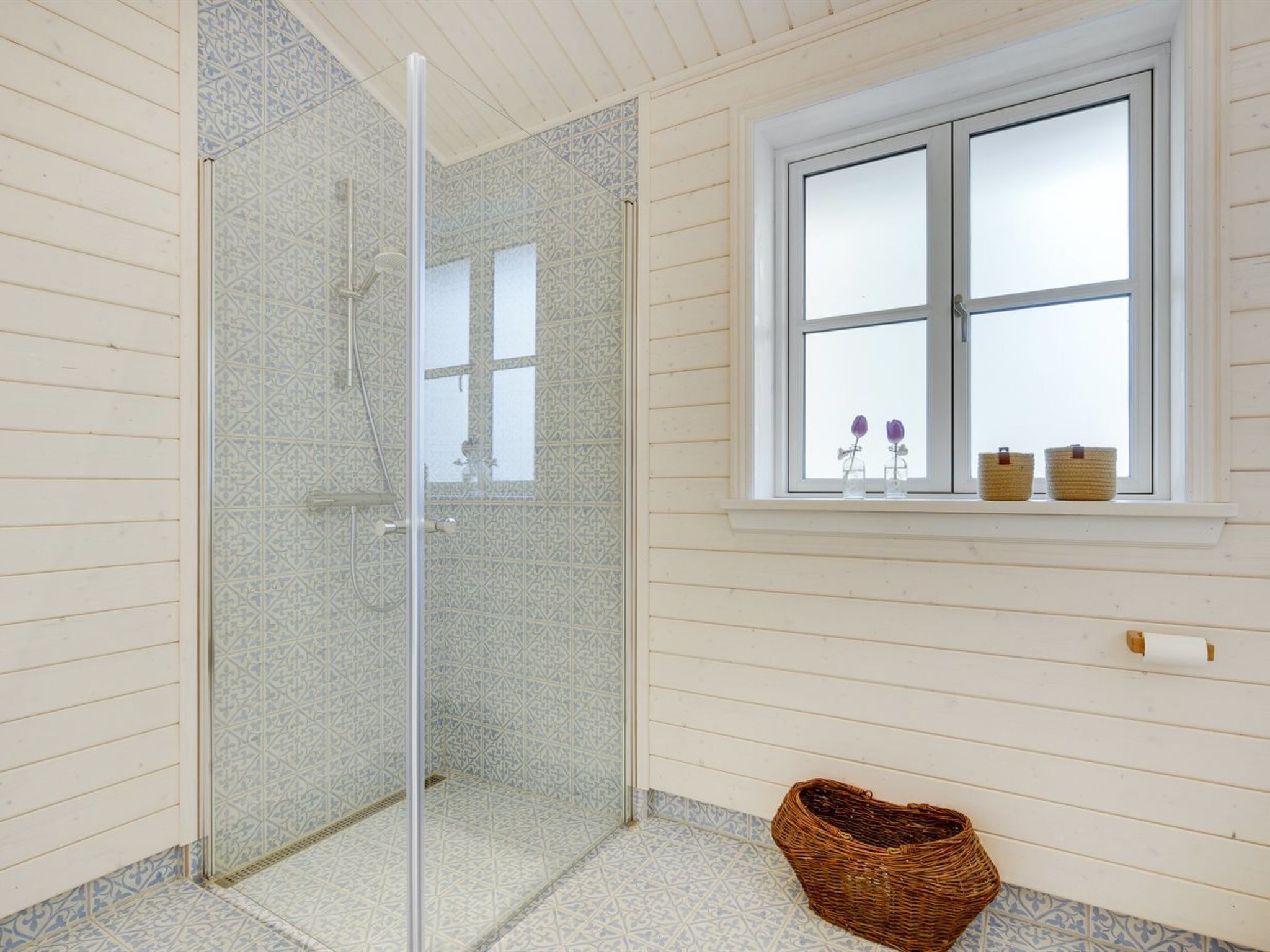Ein Badezimmer mit Duschkabine aus Glas, einem Fenster mit Körben und einem Weidenkorb auf dem Boden.