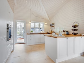 Una cocina amplia con armarios blancos, una isla de madera y un ventanal que proporciona luz natural.