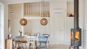 A cozy room with a wooden interior, a dining area with chairs and a table, a sofa, a hanging light fixture, and a wood-burning stove. - "Anar" - 900m from the sea by Interhome (Græsted)