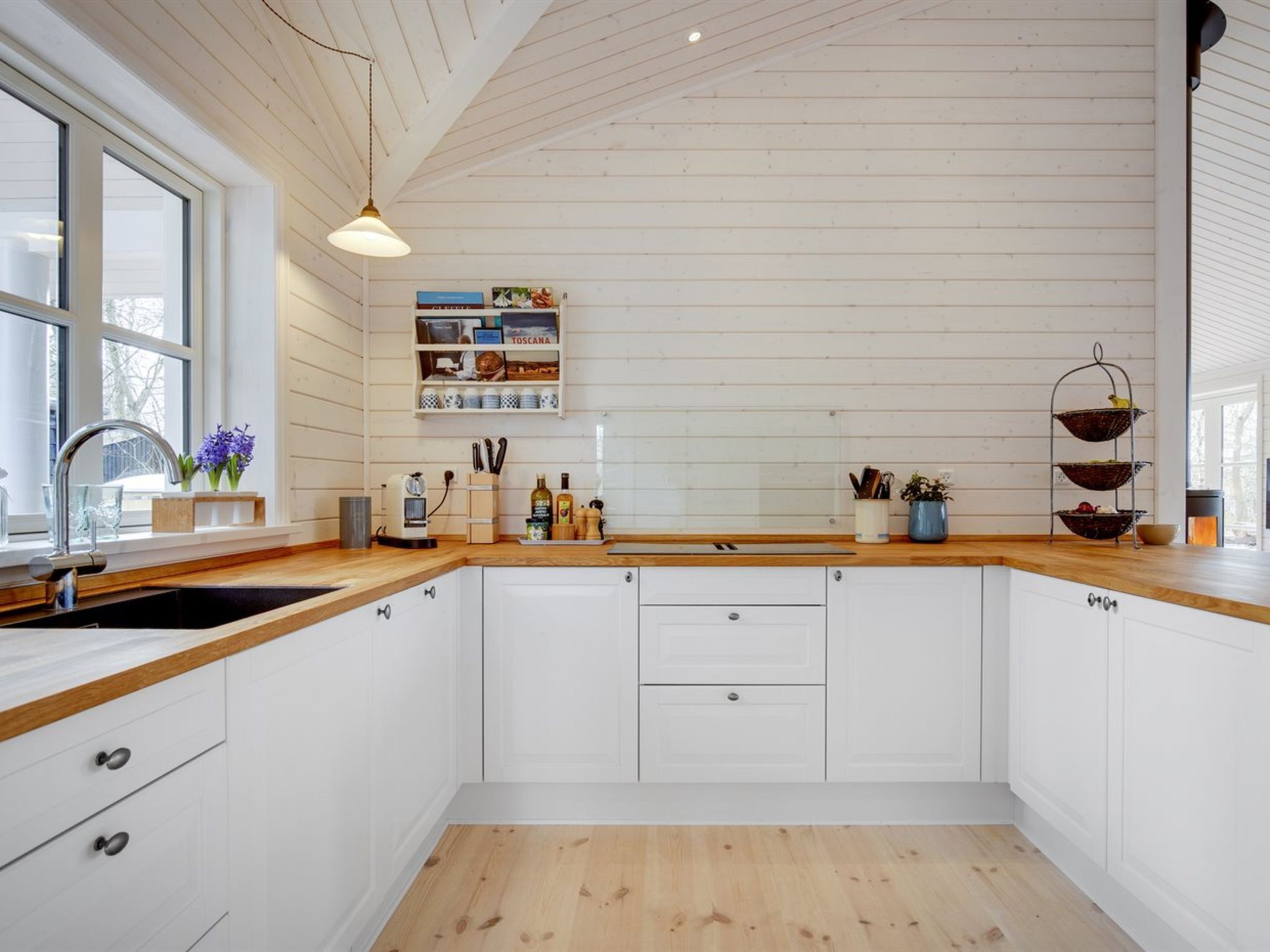 Una cocina moderna con armarios blancos, encimera de madera, estante empotrado con utensilios de cocina y una lámpara colgante.