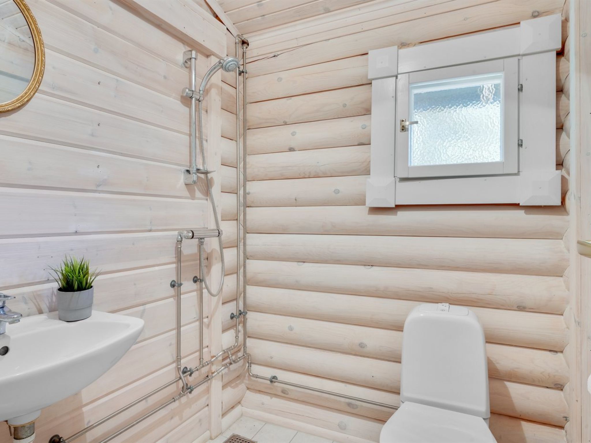 A compact wooden cabin bathroom with a sink, toilet, shower, and a small window.