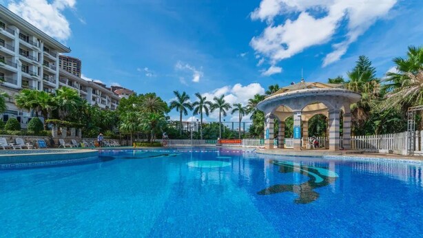 Una grande piscina con un padiglione, palme e un albergo sullo sfondo.