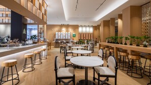 Un caffè moderno con sgabelli alti in legno, tavoli rotondi e piante in vaso.