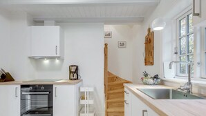 A modern kitchen with white cabinetry, a built-in oven, a coffee maker, and a wooden staircase leading to another room. - "Tabetha" - 25m from the sea by Interhome (Tisvildeleje)