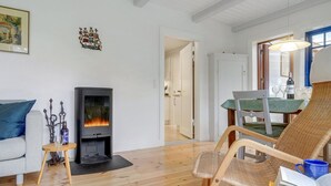 A cozy living room with a fireplace, a dining area with a table and chairs, and a wicker chair with a book and a mug. - "Tabetha" - 25m from the sea by Interhome (Tisvildeleje)