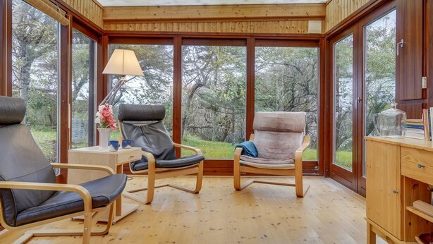 A cozy room with wooden walls and large windows, featuring two chairs, a small table with a lamp, and a wooden cabinet. - "Tabetha" - 25m from the sea by Interhome (Tisvildeleje)