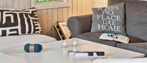 A cozy living room with a white coffee table, grey sofa, and a window with wooden paneled walls.