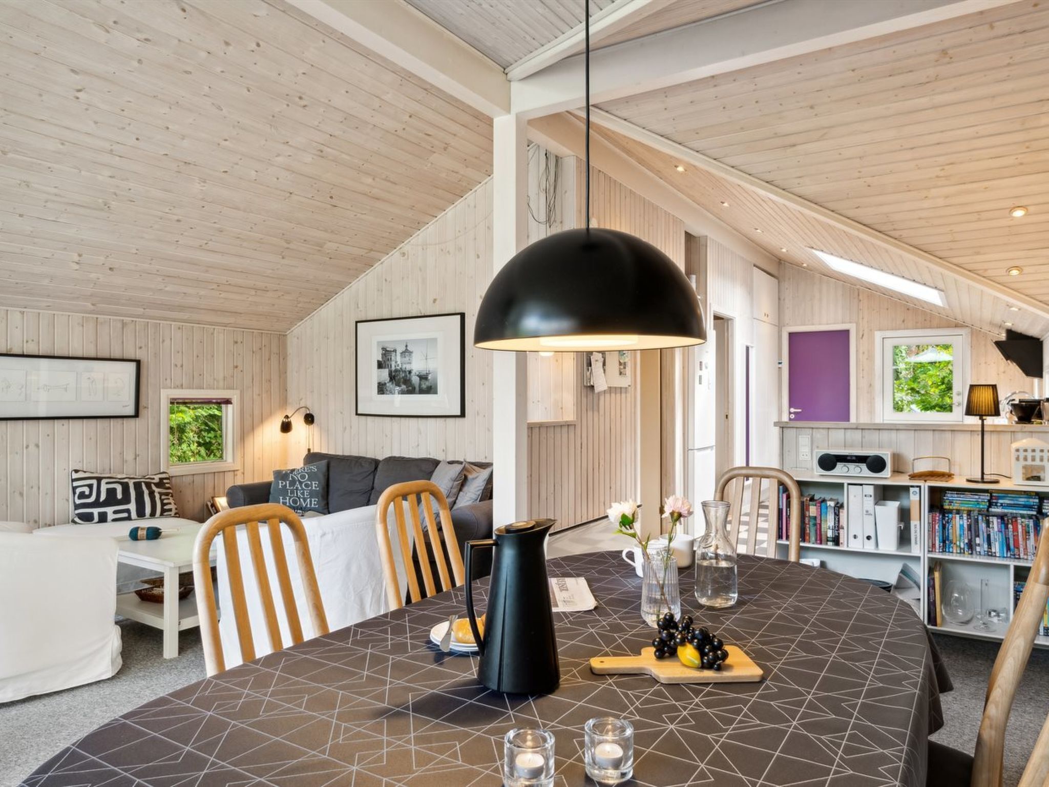 Une pièce chaleureuse et bien éclairée, avec une table à manger dressée pour deux personnes, un canapé et une bibliothèque remplie de livres.