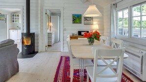 Un salon chaleureux avec une cheminée, un coin repas avec une table et des chaises, et une cuisine visible au fond.