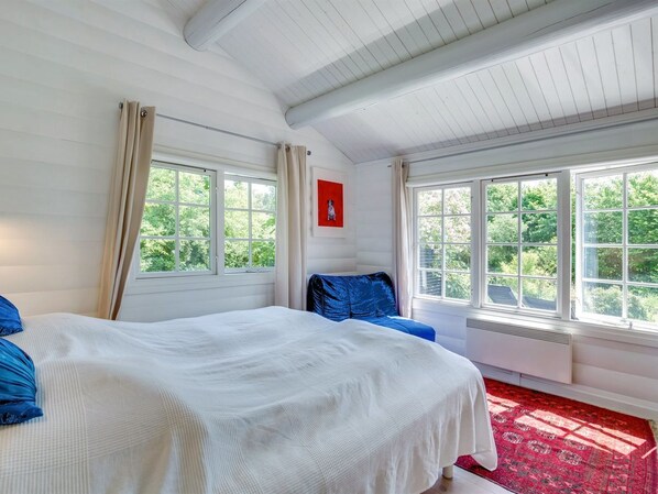 Une chambre avec un grand lit, deux fenêtres, un cadre photo rouge et une moquette rouge.