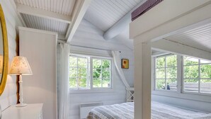 Une chambre avec un lit superposé, une table de chevet avec une lampe et de grandes fenêtres avec des rideaux.