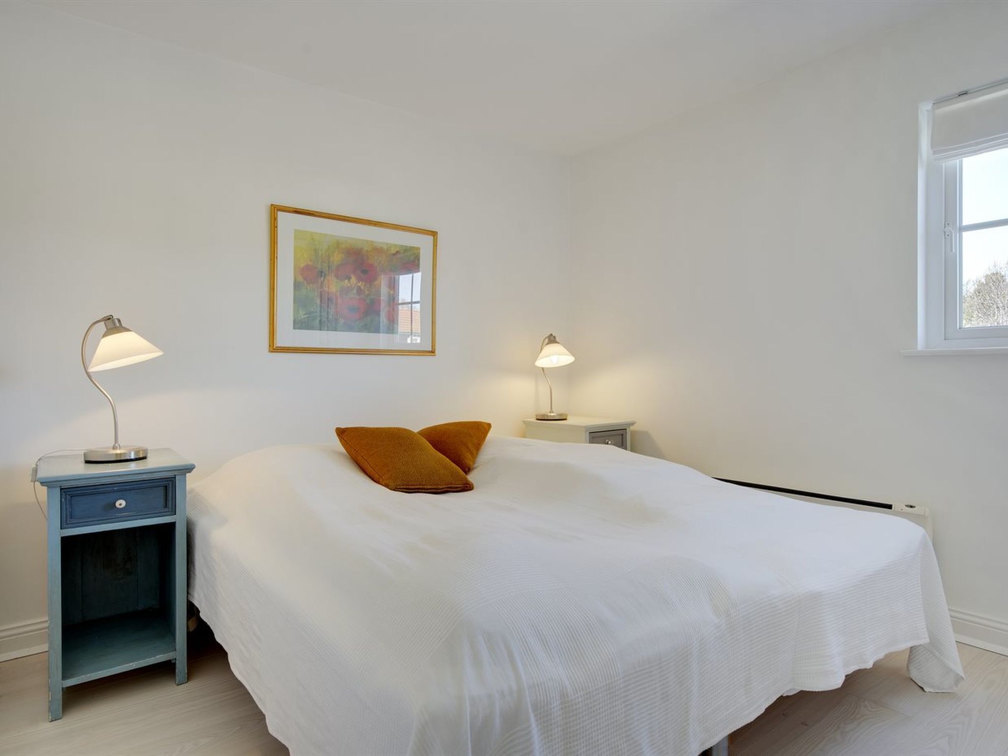 Un dormitorio con una cama grande, dos mesitas de noche con lámparas, un aparador y un cuadro en la pared.