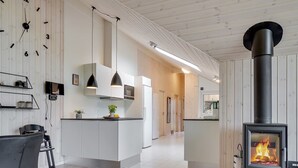 A modern kitchen with a central island, pendant lighting, and a wood-burning stove.