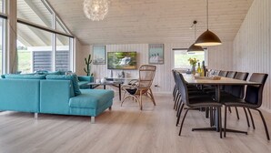 A spacious living area with a teal sofa, dining table with chairs, and a television.