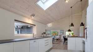 A modern kitchen with a skylight, white cabinetry, and a dining area with a table and chairs.
