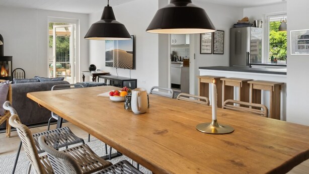 A modern kitchen with a wooden dining table, black pendant lights, and a view of the outdoors.
