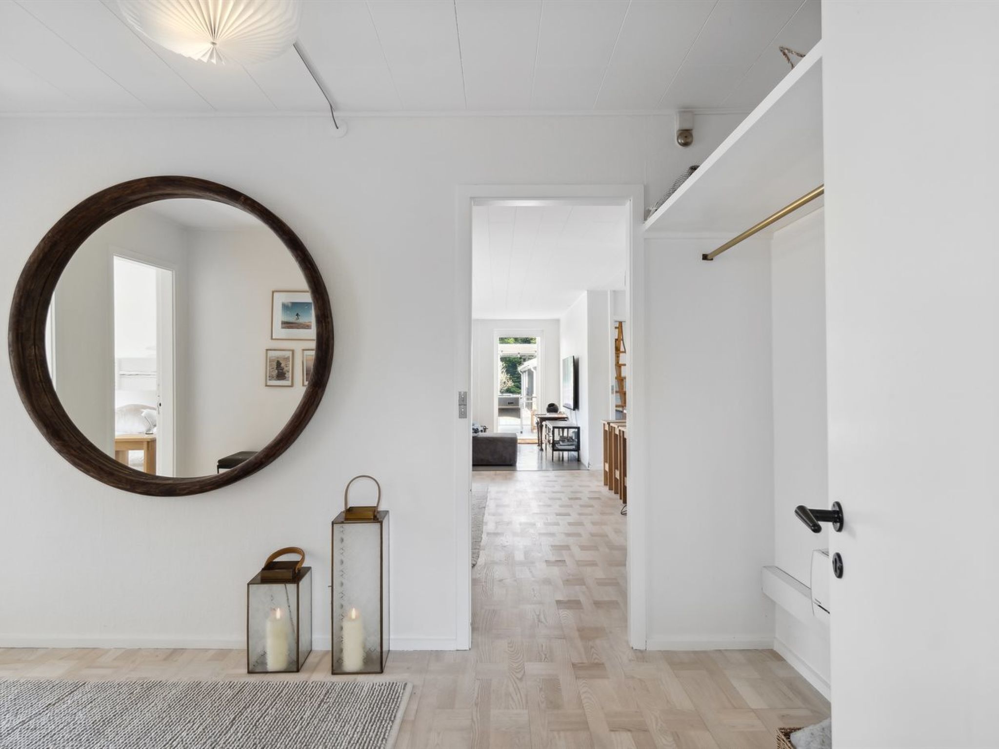 A modern interior with a large round mirror, two candle lanterns, and a hallway leading to a dining area.