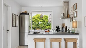 A modern kitchen with a large window, wooden stools, and a stainless steel refrigerator.