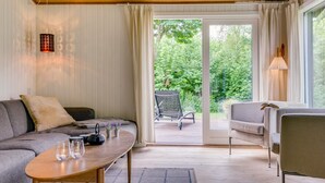 Ein modernes Wohnzimmer mit einer Couch, einem Couchtisch und einem Sessel. Eine Glastür verschiebt sich zu einem Außenbereich mit einem Stuhl und einem Tisch.