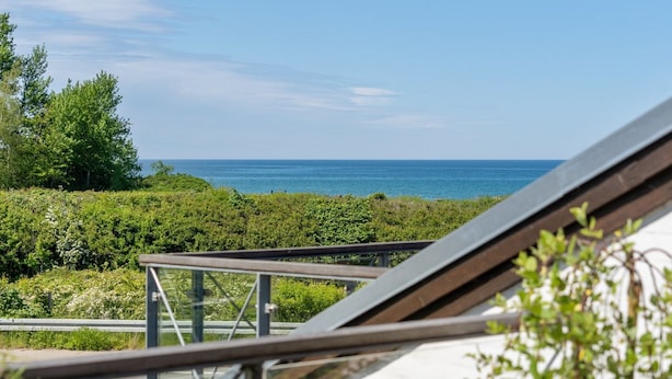 Een balkon met uitzicht op de zee, omringd door groen.