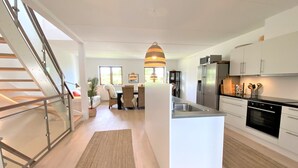 Een moderne keuken met een centraal eiland, roestvrijstalen apparatuur en een eethoek met rieten stoelen.