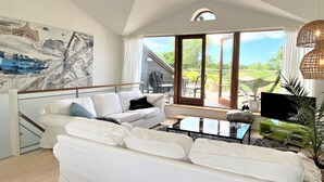 Een moderne woonkamer met een witte bank, een glazen salontafel en een groot schilderij aan de muur.