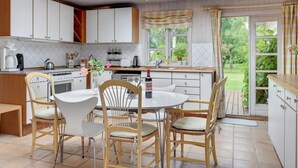 Una cucina moderna con mobili bianchi, un tavolo da pranzo con sedie e vista sul giardino tramite ampie finestre.