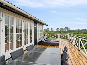 Eine Terrasse mit einem Glastisch, Stühlen, Holzboden und einem weißen Geländer.