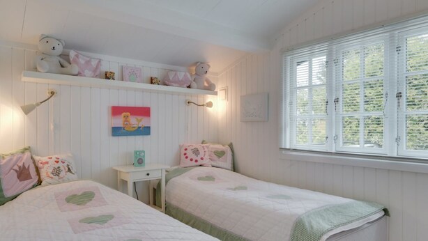Ein gemütliches Schlafzimmer mit zwei Betten, einem Regal mit Dekoration, einem Gemälde und einem Fenster mit Jalousien.